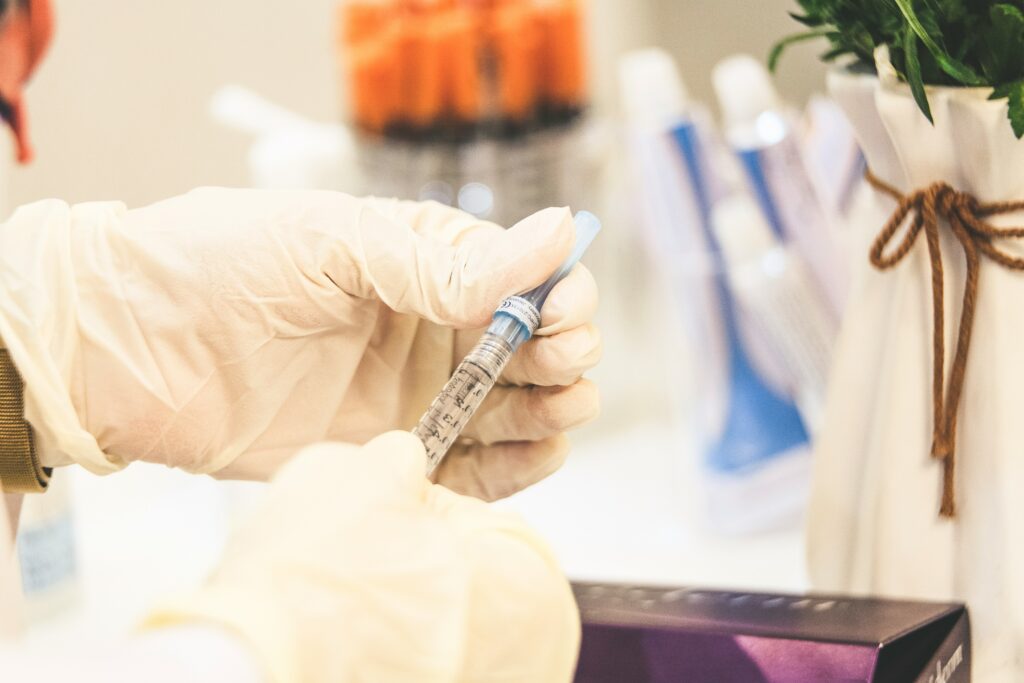 Gloved hand holding a syringe for precision cosmetic treatment against a soft-focus medical spa backdrop, representing Santa Fe neurotoxin and filler services.