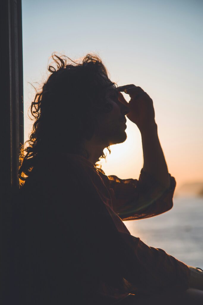 Woman gazing out a window at sunset, reflecting on the relief from chronic migraines through neurotoxin therapy in Santa Fe.